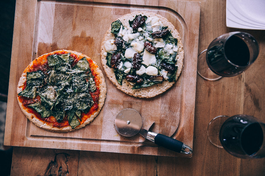 Pizzas auf einem Holzbrett mit einem Pizzaschneider und zwei Weingläser